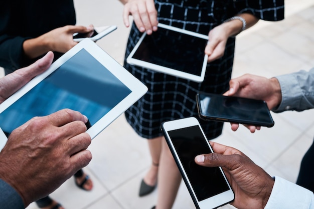 Close-up of diverse hands using smartphones and tablets in a bustling urban setting, representing the digital transformation and innovation in the service sector.