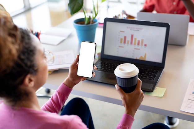 A person holding a smartphone showing a budgeting app, with charts and graphs illustrating income and expenses. The background is a bright and modern home office.
