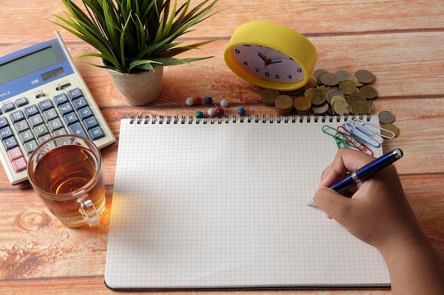 A person meticulously writing down expenses in a budget planner, surrounded by coins and bills, highlighting the importance of budgeting and financial planning.