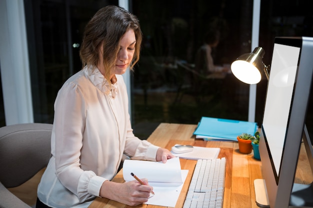 A person is shown working diligently on their computer, using the official income tax software, with a notepad and pen nearby for notes. The setting is a well-lit and organized home office.