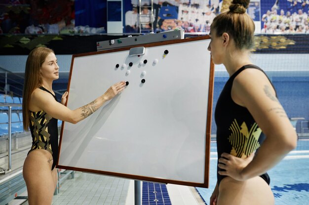 A coach reviewing a swimmer's form with a whiteboard displaying stroke analysis, pool setting, professional equipment, focused interaction, bright daylight.