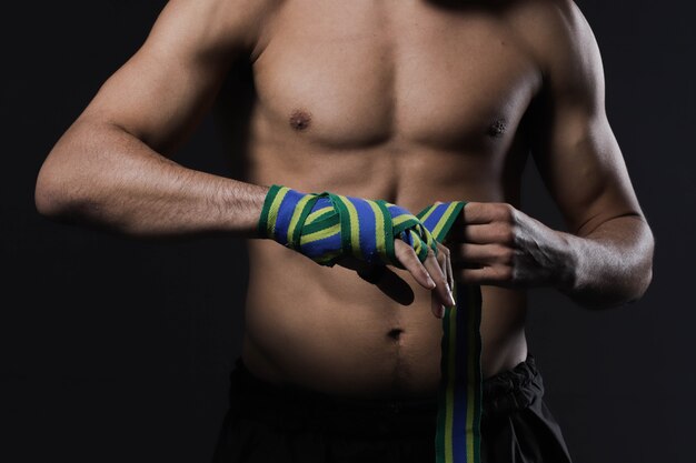 A close-up shot of a Brazilian MMA fighter's hands wrapped in tape, showcasing the preparation and attention to detail before a fight. The fighter's determined expression is visible, with sweat and grit adding to the intensity. The background is blurred to emphasize the subject.