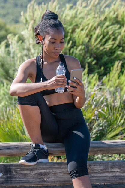 A Brazilian female athlete drinking water from a bottle, resting after a training session on a running track, with a focused expression.