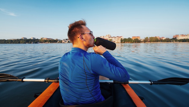 A side-view shot of a rowing coach using a megaphone to instruct a team of rowers in a boat on the water.