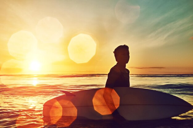 A surfer meditating on the beach before a competition. The sun is rising in the background, and the surfer has a peaceful expression on their face.