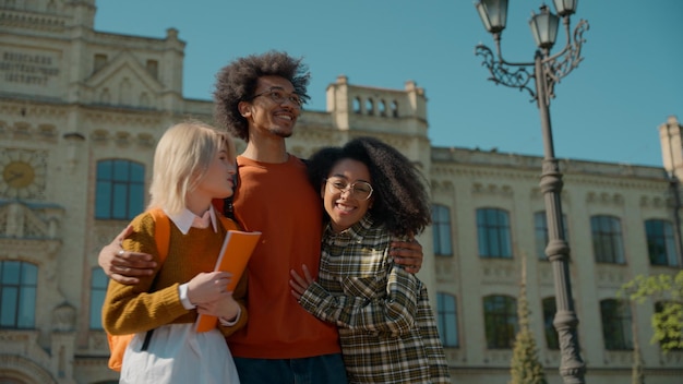 A diverse group of Brazilian college students chatting and laughing while walking together across a sunny university campus, with classic architecture in the background.