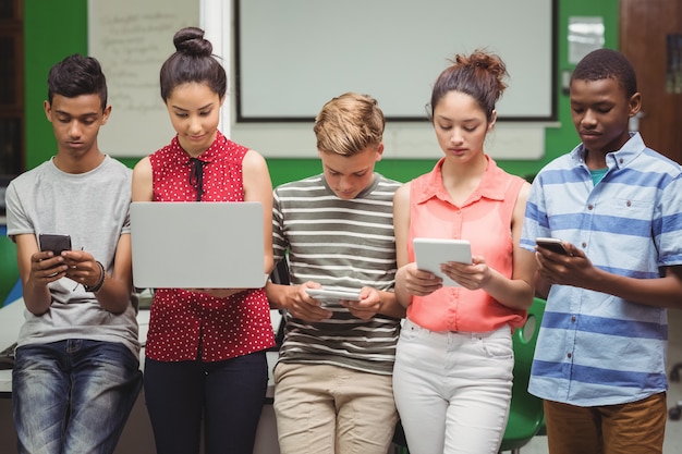 A diverse group of high school students using tablets and laptops in a classroom, working on a collaborative digital project. The focus is on technology and teamwork, suggesting a modern, engaging learning environment.
