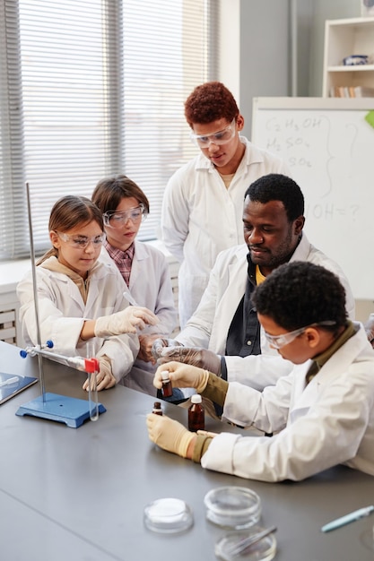 Students of different ethnicities working together in a science lab, conducting an experiment with test tubes and beakers. Some students are wearing lab coats and safety goggles, while others are taking notes. The lab is well-equipped and modern, reflecting a commitment to STEM education.