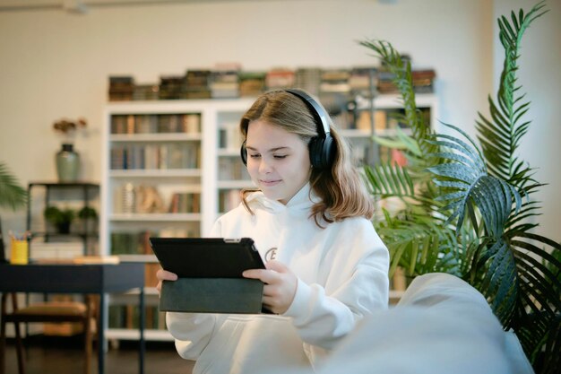 A student wearing headphones taking notes while watching an online lecture on a tablet, set against a backdrop of a comfortable home office.