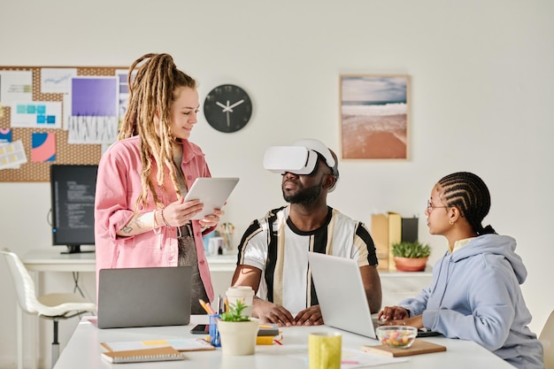 A diverse group of students collaborating on a project using augmented reality tools in a modern classroom setting. The scene emphasizes teamwork, innovation, and engagement with digital technology.