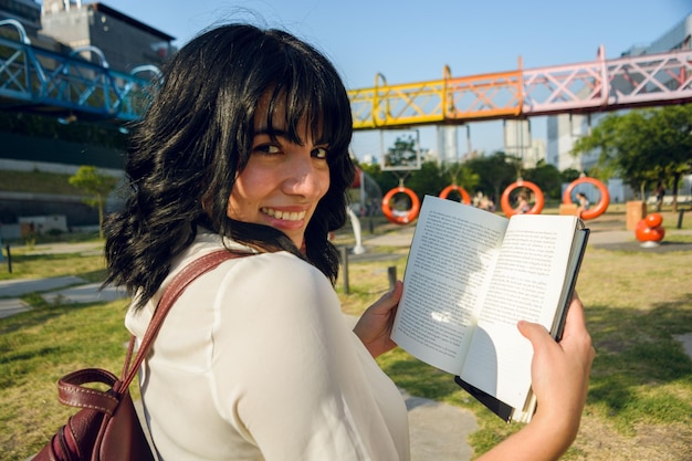 Close-up shot of a young Brazilian student smiling and holding a textbook on a university campus in Sydney, Australia, with the Sydney Opera House visible in the background.
