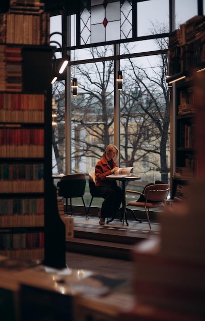 Scene inside a library at Oxford University, England, with a Brazilian student studying at a wooden table, surrounded by old books and high bookshelves. Sunlight streams through the large windows.