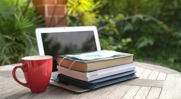 a stack of well-worn textbooks on a wooden table, a digital tablet displaying an online educational platform, a pen and notebook open beside them, capturing a blend of traditional and modern learning resources.