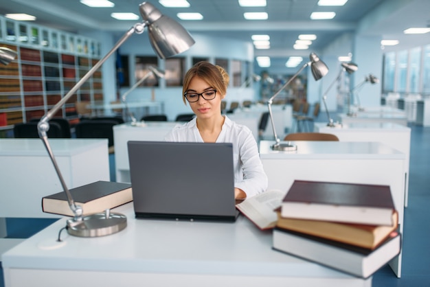A medium shot of a female student working on a laptop in a brightly lit, modern university lab, surrounded by scientific equipment and books, with a focused expression.