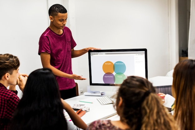 A diverse group of students collaborating on a project using a large touch screen display, with the teacher providing guidance and support.
