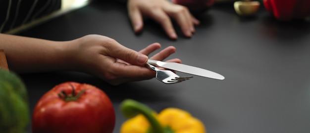 A close-up shot of hands demonstrating a specific knife technique on a vegetable during an online cooking class. The video screen showing the instructor is visible in the background.