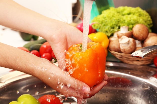 A close-up of hands washing fresh produce (fruits and vegetables) under running water in a kitchen sink, emphasizing the importance of cleaning before consumption.