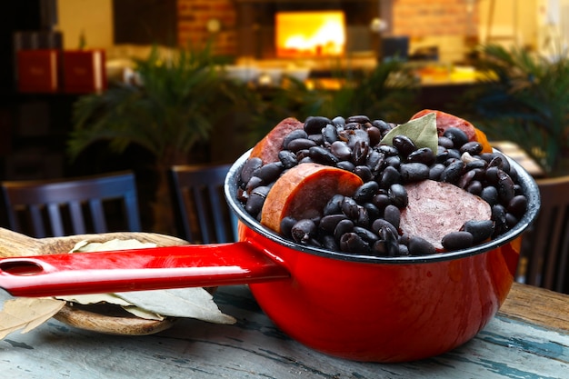 A close-up shot of a feijoada being served in a clay pot, with visible ingredients like black beans, sausages, pork cuts, and condiments, highlighting the richness and complexity of Brazilian cuisine.